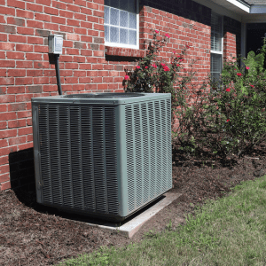 A green air conditioner sitting outside of a brick house.